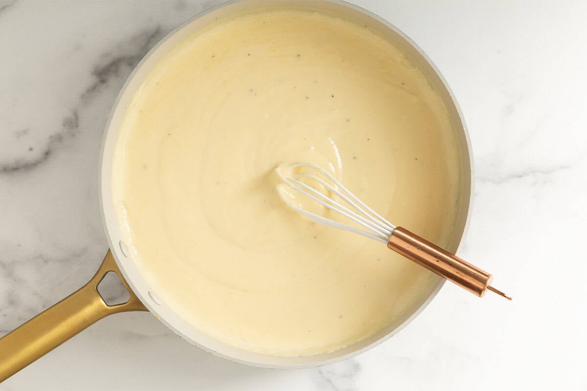 Whisk stirring mac and cheese sauce in pan.