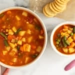 Vegetable soup in two bowls with crackers and spoons.