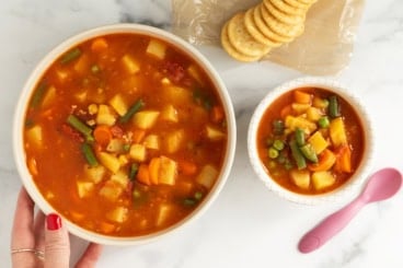 Vegetable soup in two bowls with crackers and spoons.