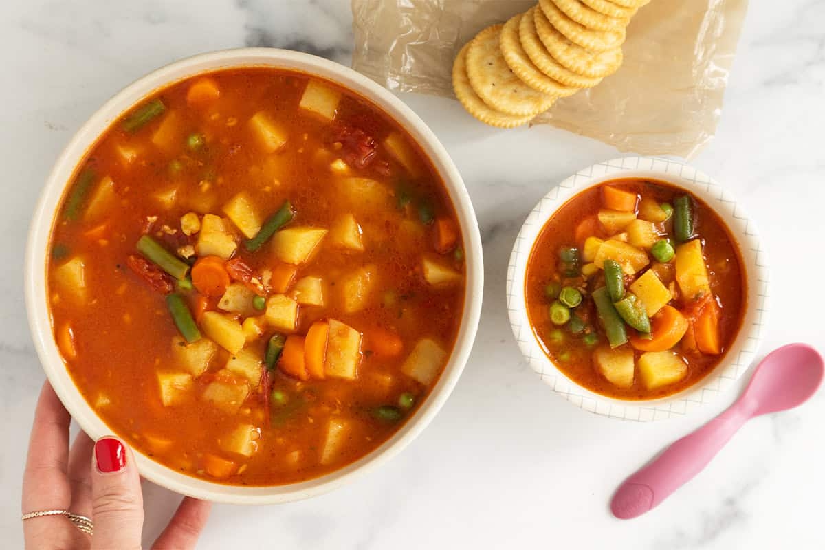 Vegetable soup in two bowls with crackers and spoons.