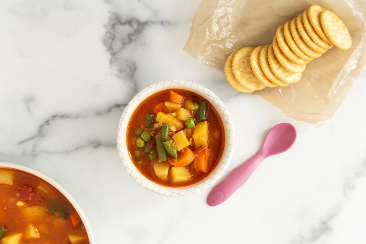 Vegetable soup in bowl with crackers on side.