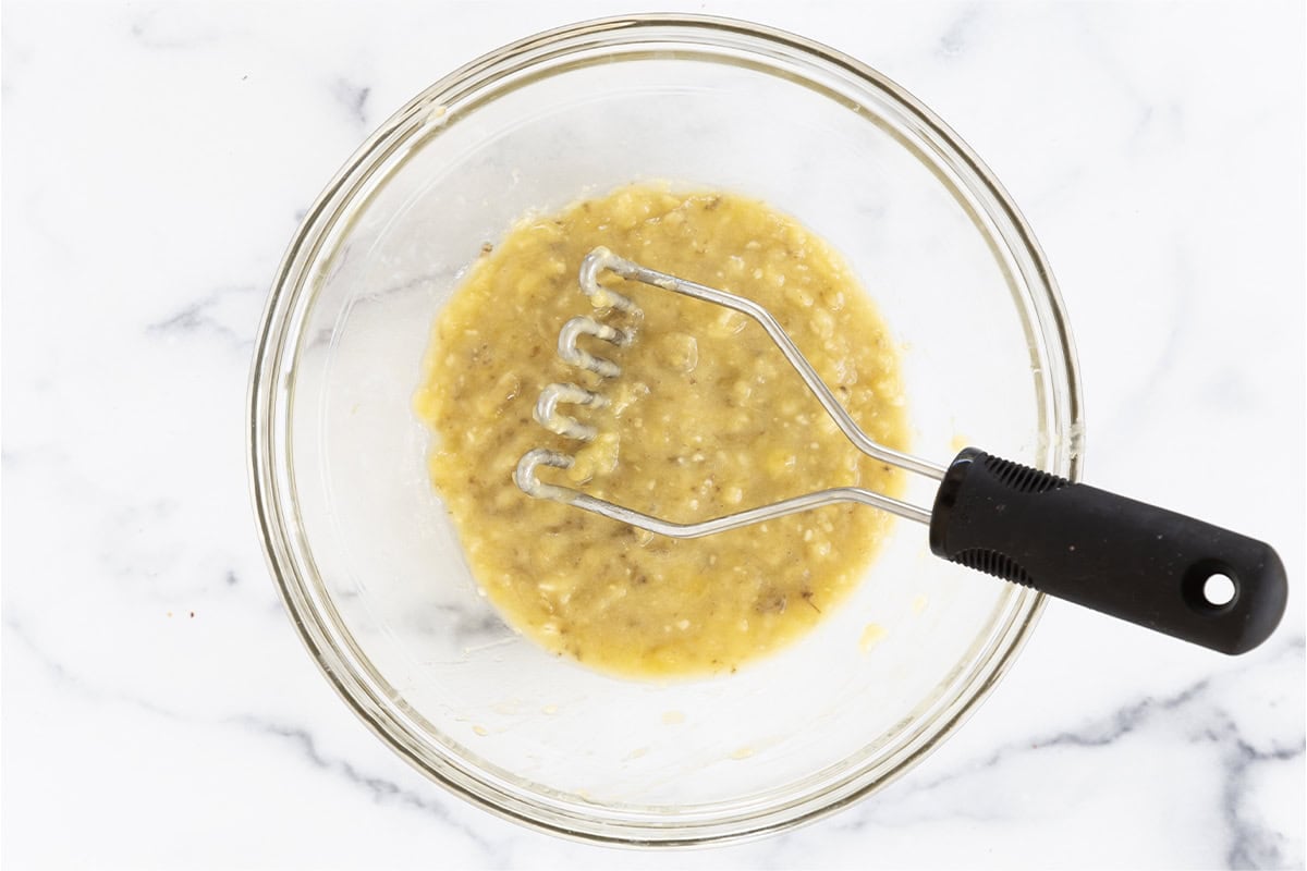 Banana being mashed in bowl for banana oatmeal bars. 