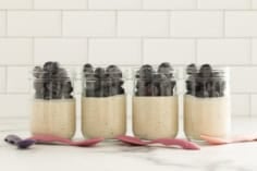 Coconut overnight oats topped with blueberries in four glass jars.