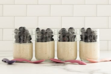 Coconut overnight oats topped with blueberries in four glass jars.