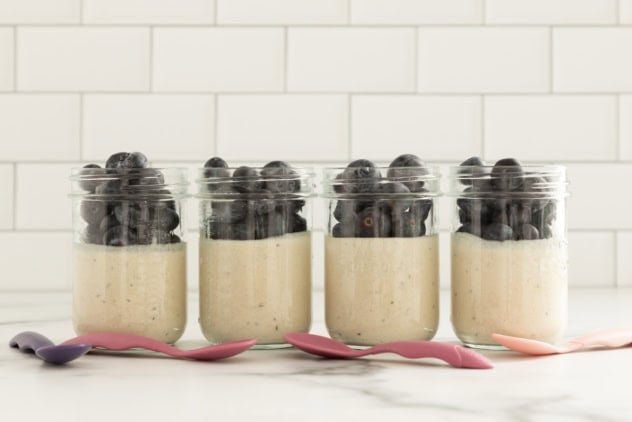 Coconut overnight oats topped with blueberries in four glass jars.