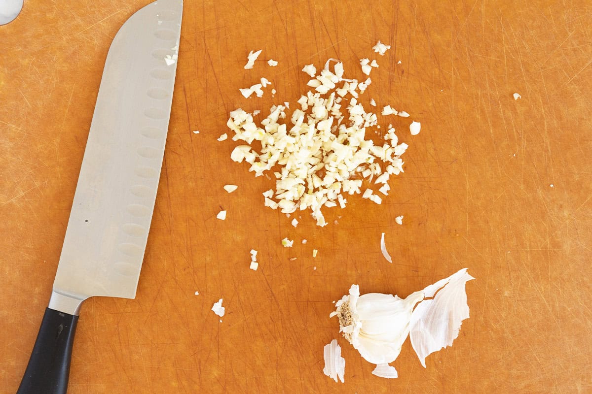 Chopping garlic on cutting board for yogurt sauce.