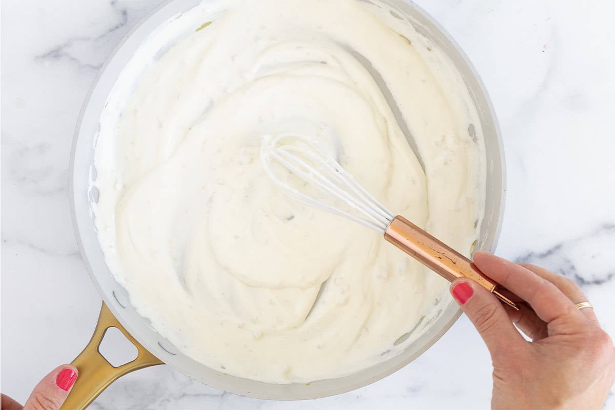 Yogurt sauce in pan with whisk.