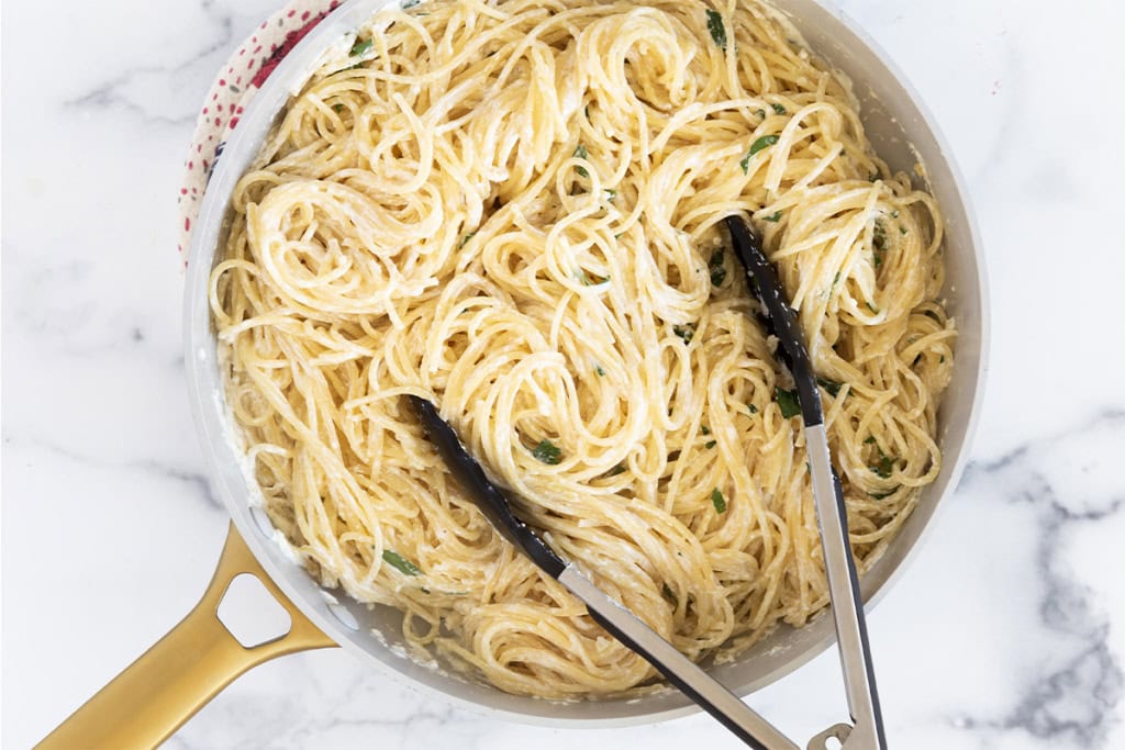 Pasta with yogurt sauce in pan with thongs.