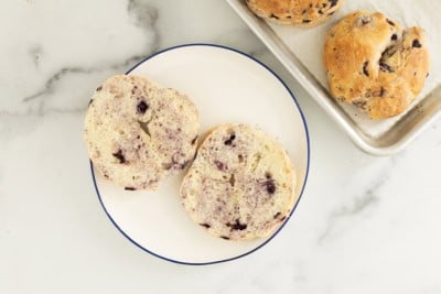 Blueberry bagel cut open on white plate.