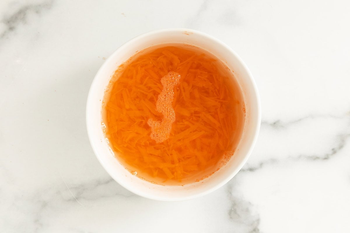 Shredded carrot in bowl with water.