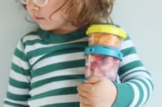 toddler holding three containers of snacks.