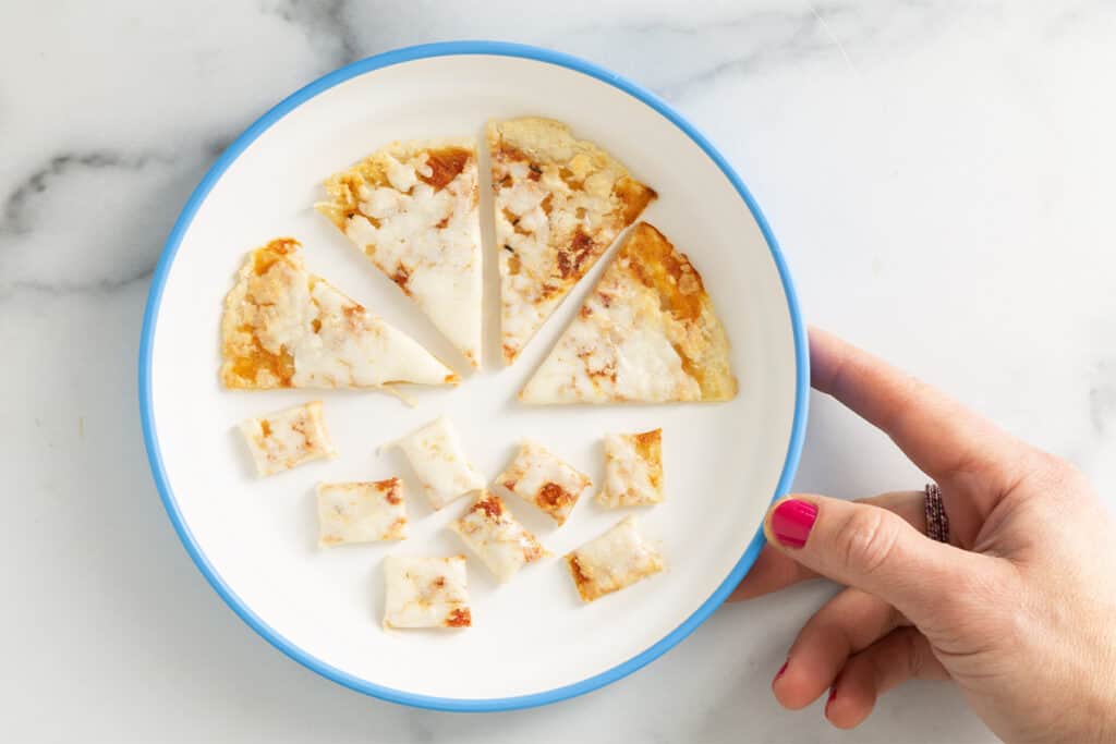 diced baby pizza on white plate with blue trim with hand.