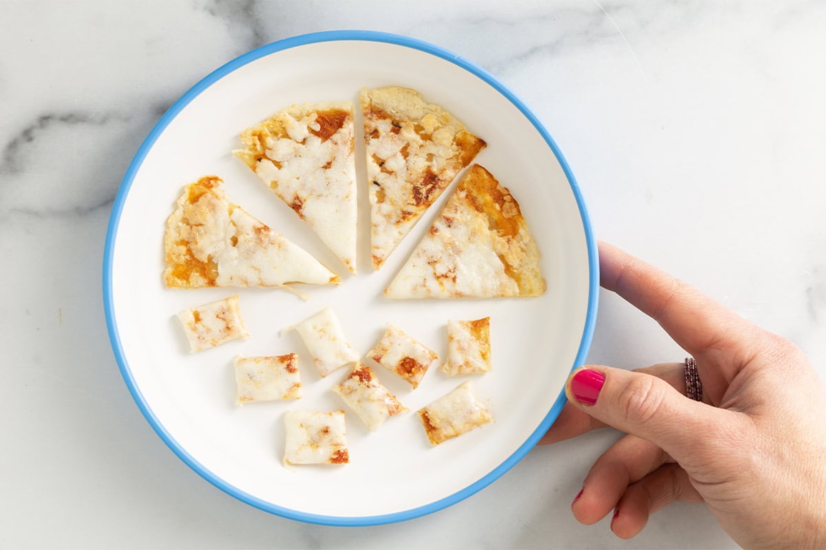diced baby pizza on white plate with blue trim with hand.