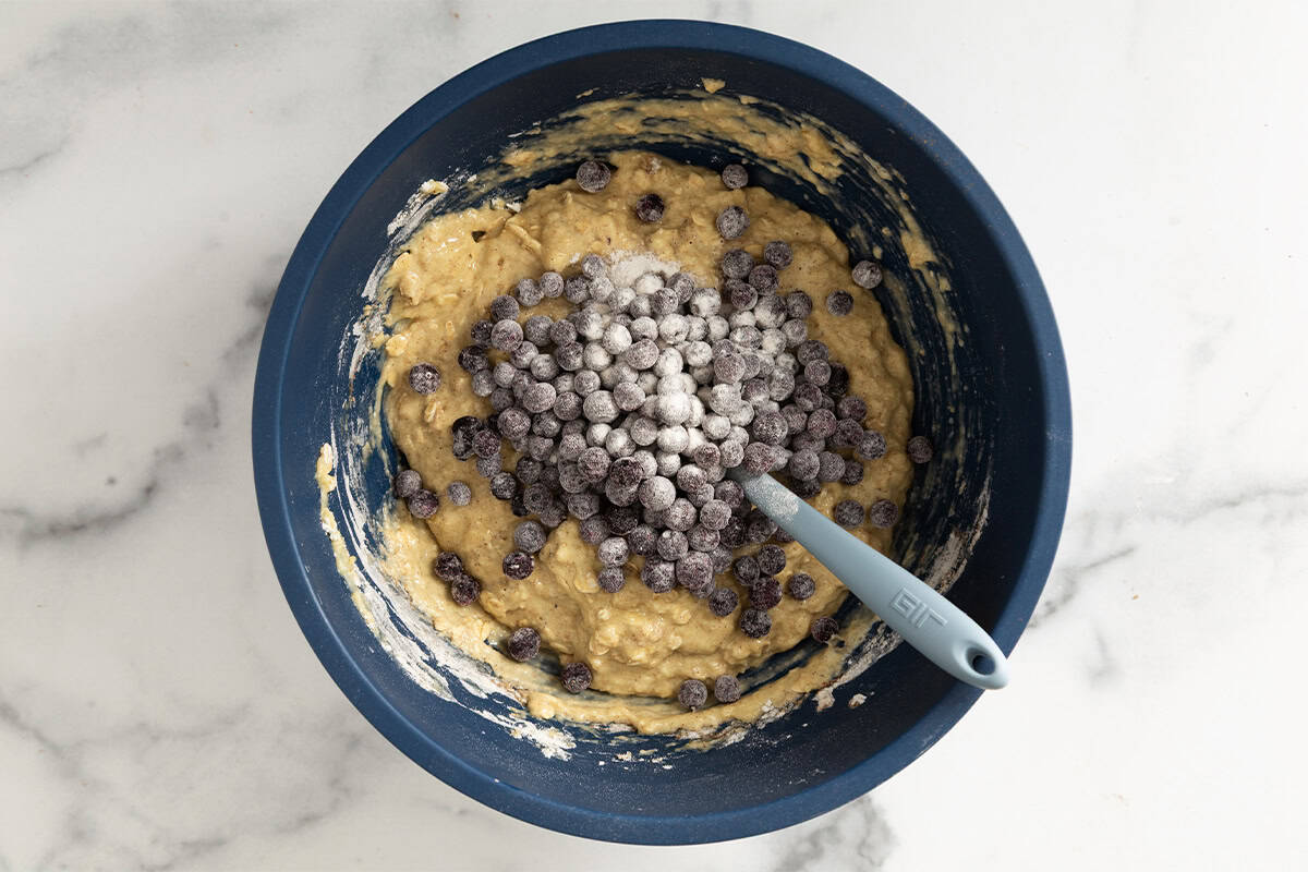 Batter with blueberries being added for blueberry oatmeal muffins.
