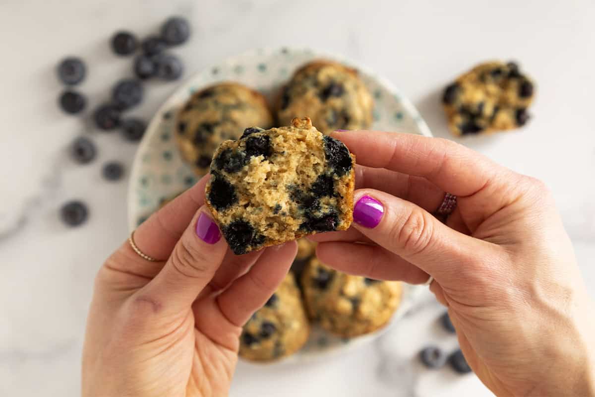 Hands holding blueberry oatmeal muffin.