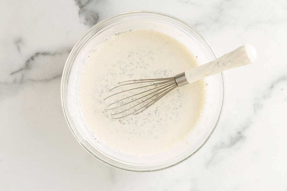Ingredients for chia pudding in glass bowl with whisk.
