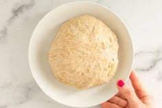 no knead pizza dough in white bowl with hand.