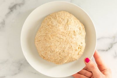 no knead pizza dough in white bowl with hand.