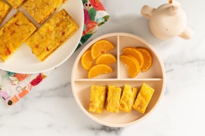 Vegetable egg bake on two plates with oranges.