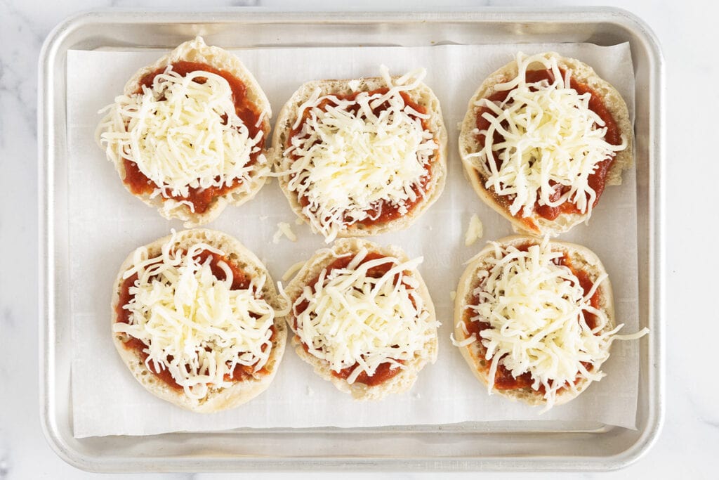 mini pizzas with sauce and cheese on baking pan.