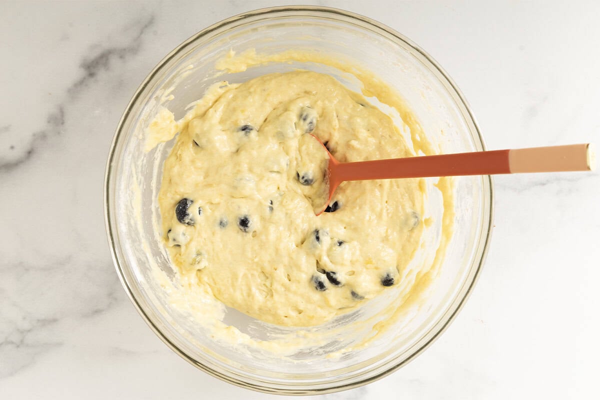 Adding blueberries to batter in glass bowl.