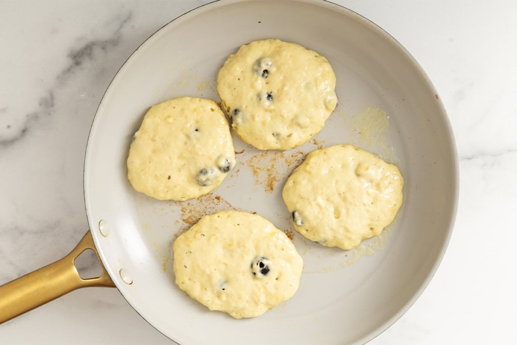Blueberry banana pancakes in pan before flipping.