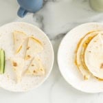 Cheese quesadillas on two white plates with cucumber sticks.