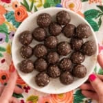 Chocolate date balls on white plate with hands holding plate.