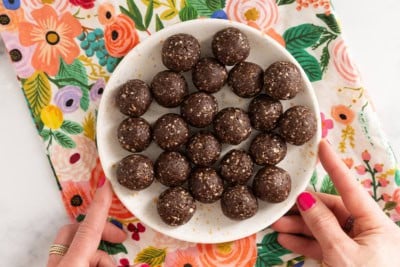 Chocolate date balls on white plate with hands holding plate.