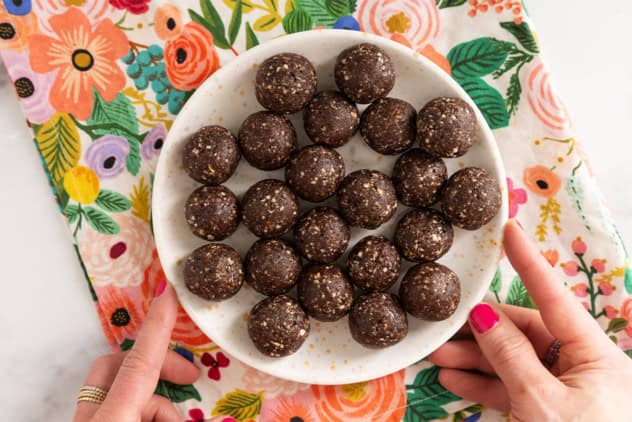 Chocolate date balls on white plate with hands holding plate.