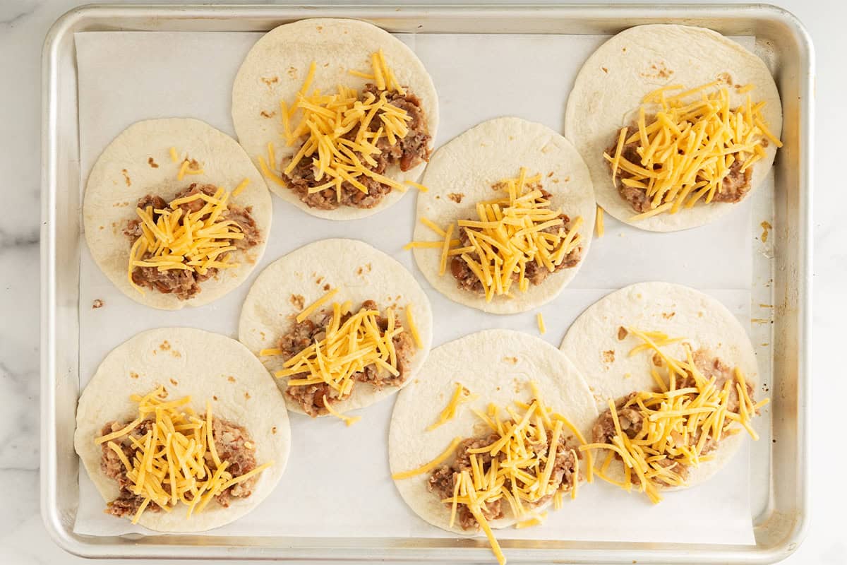 Mini tacos with cheese and beans on baking sheet.