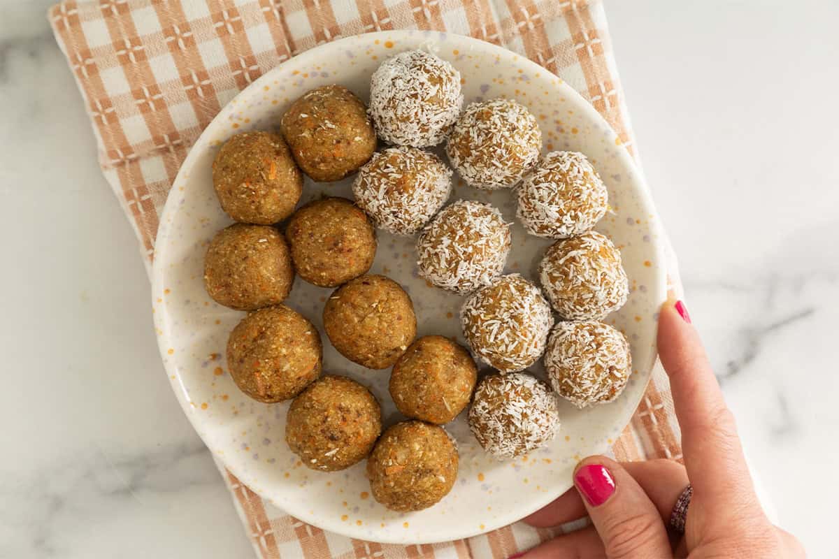 Hand holding plate of carrot balls. 