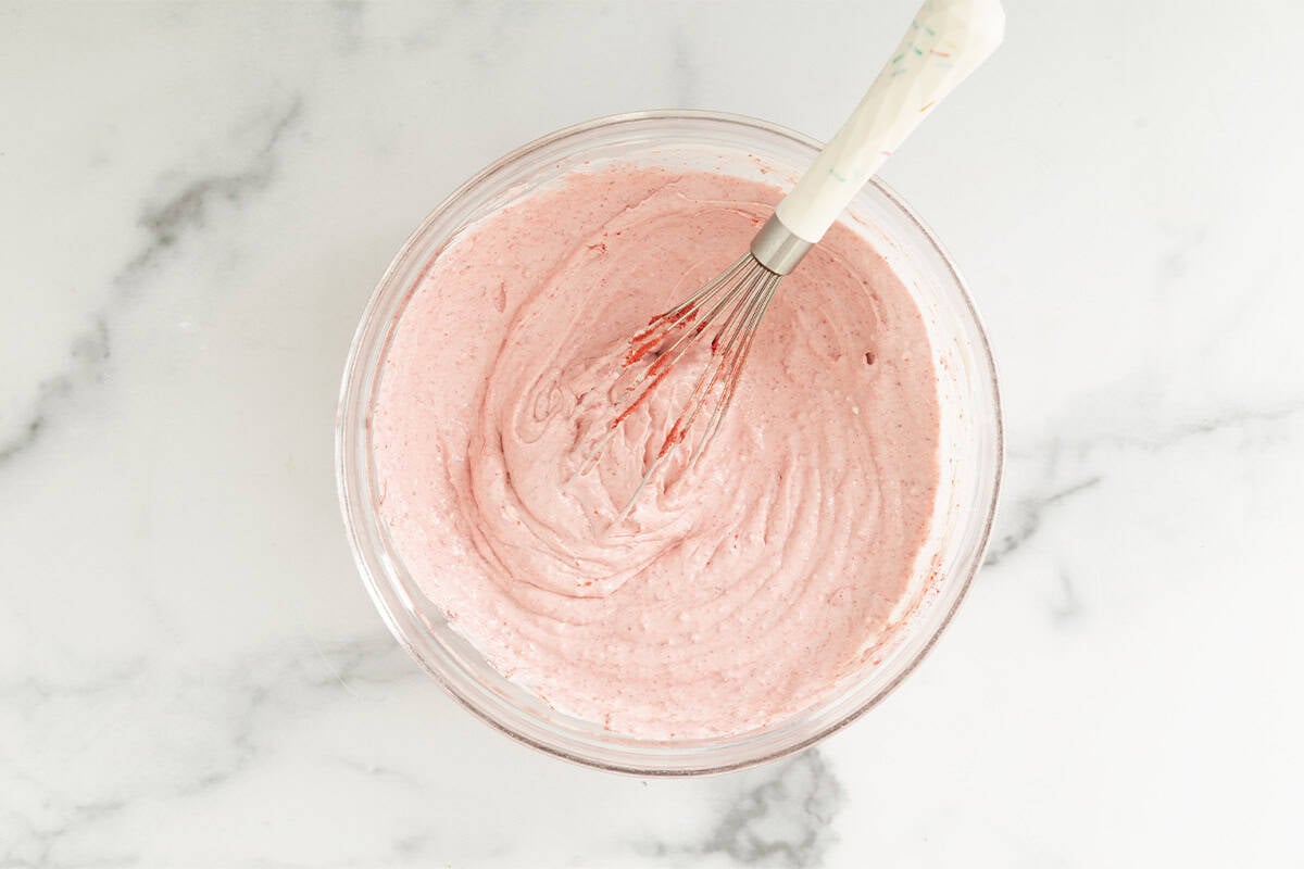 Strawberry cheesecake mixture in glass bowl with whisk.