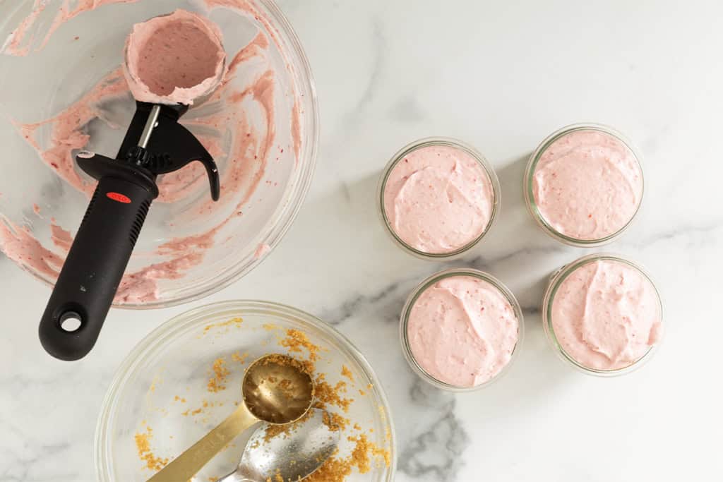 No bake strawberry cheesecake being make in small glasses.