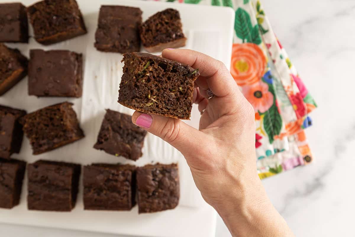 Zucchini chocolate cake cut into squares with hands holding a square.