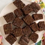 Zucchini chocolate cake cut into squares on white plate.