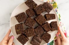 Zucchini chocolate cake cut into squares on white plate.