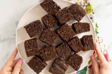 Zucchini chocolate cake cut into squares on white plate.