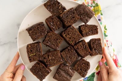 Zucchini chocolate cake cut into squares on white plate.