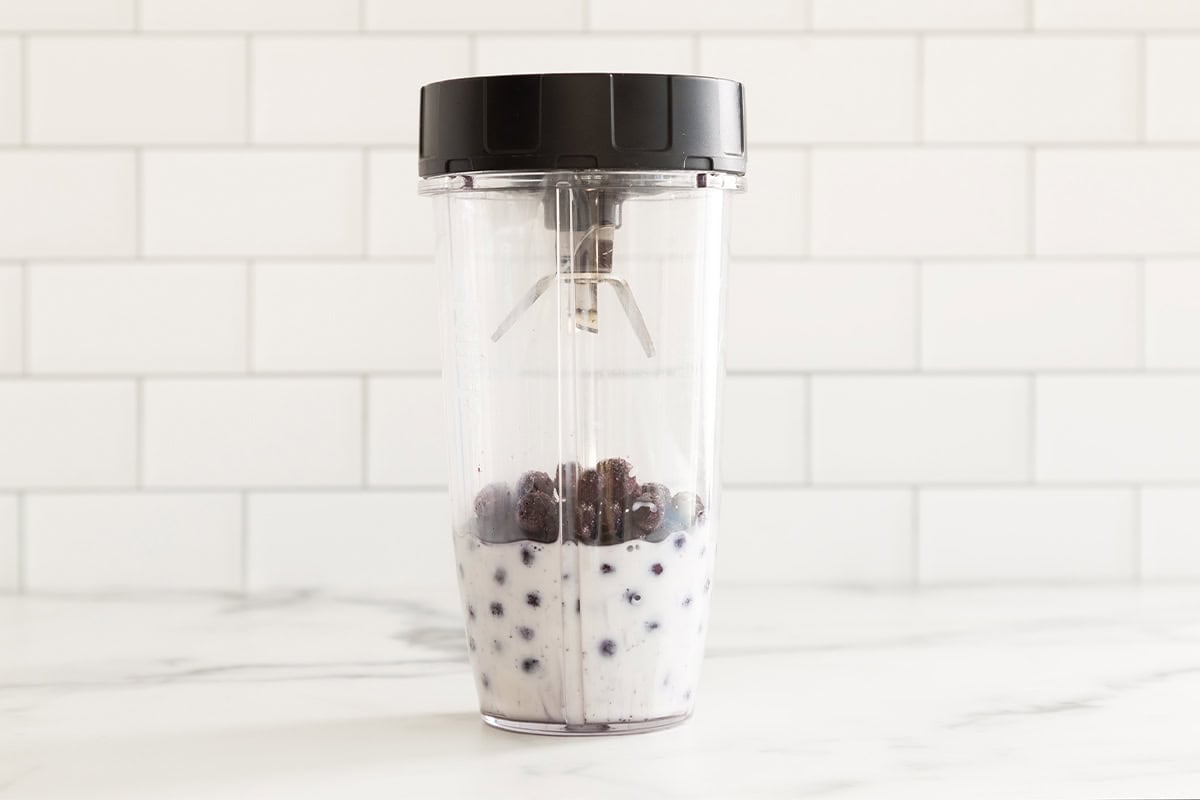 Milk and blueberries in blender for blueberry milk.