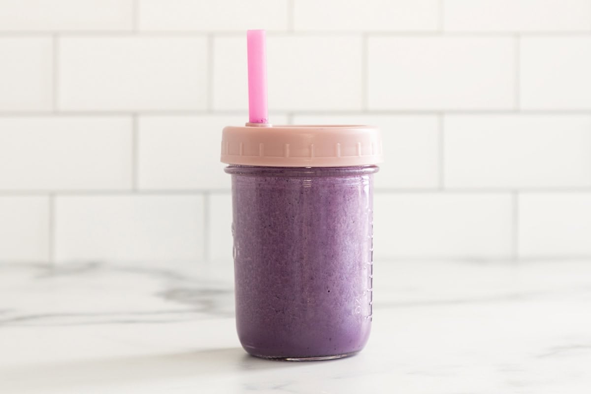 Blueberry milk in glass jar with lid and straw.