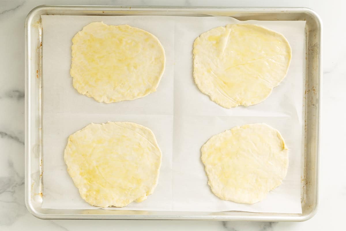 pizza dough in four pizzas spread on baking sheet.