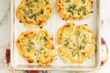 Broccoli pizza cut into pieces on baking sheet.