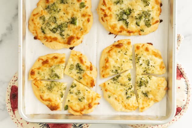 Broccoli pizza cut into pieces on baking sheet.