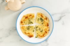 Broccoli pizza in four pieces on white plate.