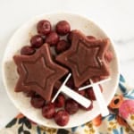 Cherry popsicles on white plate with cherries.