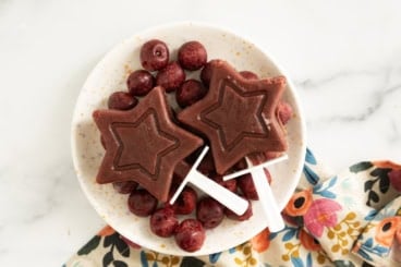 Cherry popsicles on white plate with cherries.