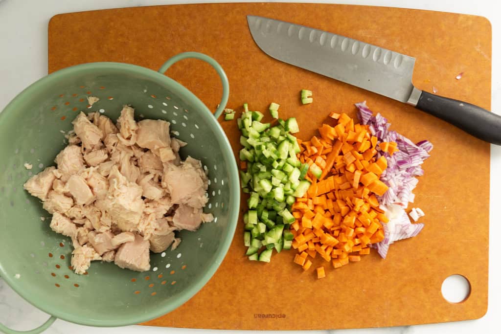 Veggies and chicken being chopped on cutting board for chicken mac salad.