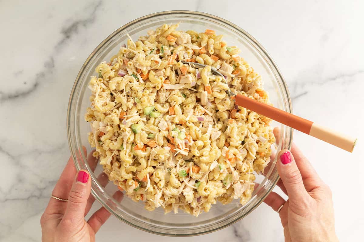Chicken mac salad in glass bowl with hands holding bowl.