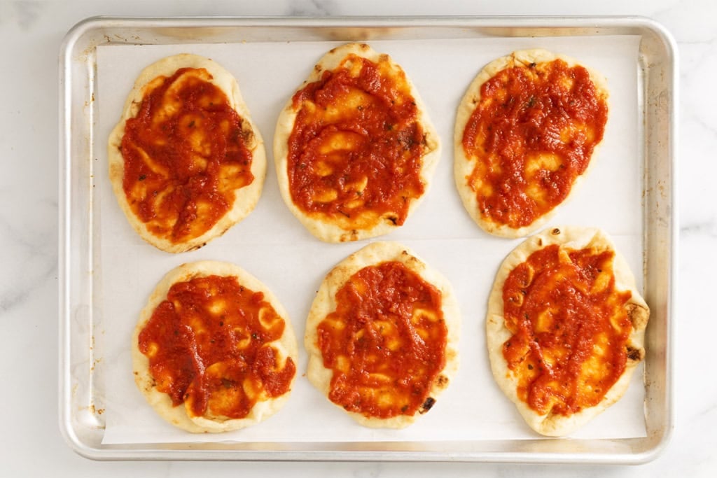 Sauce on naan bread on baking sheet.